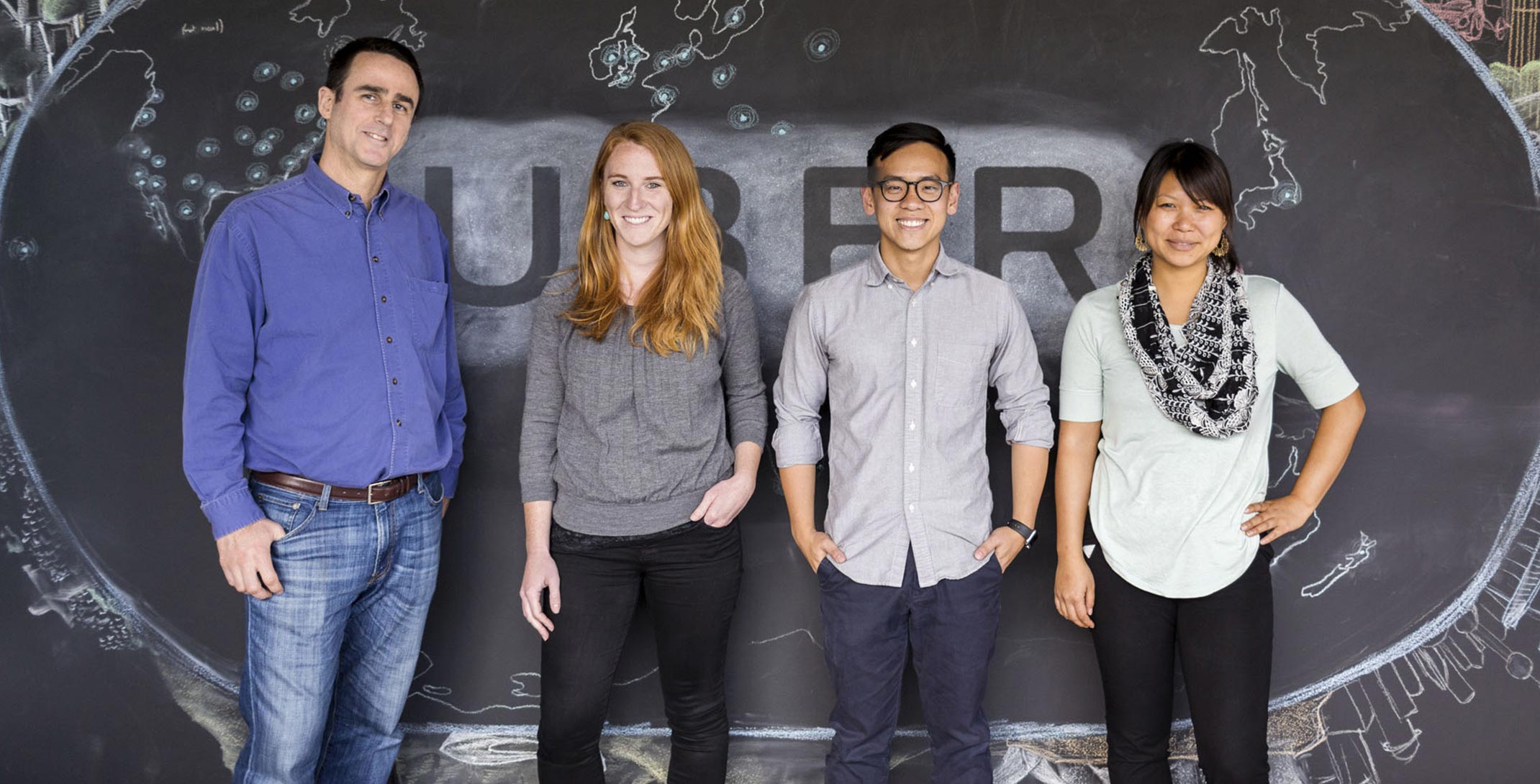 Four team members stand in front of a chalkboard wall, with a drawing of the Uber logo and a map of the cities in which it operates