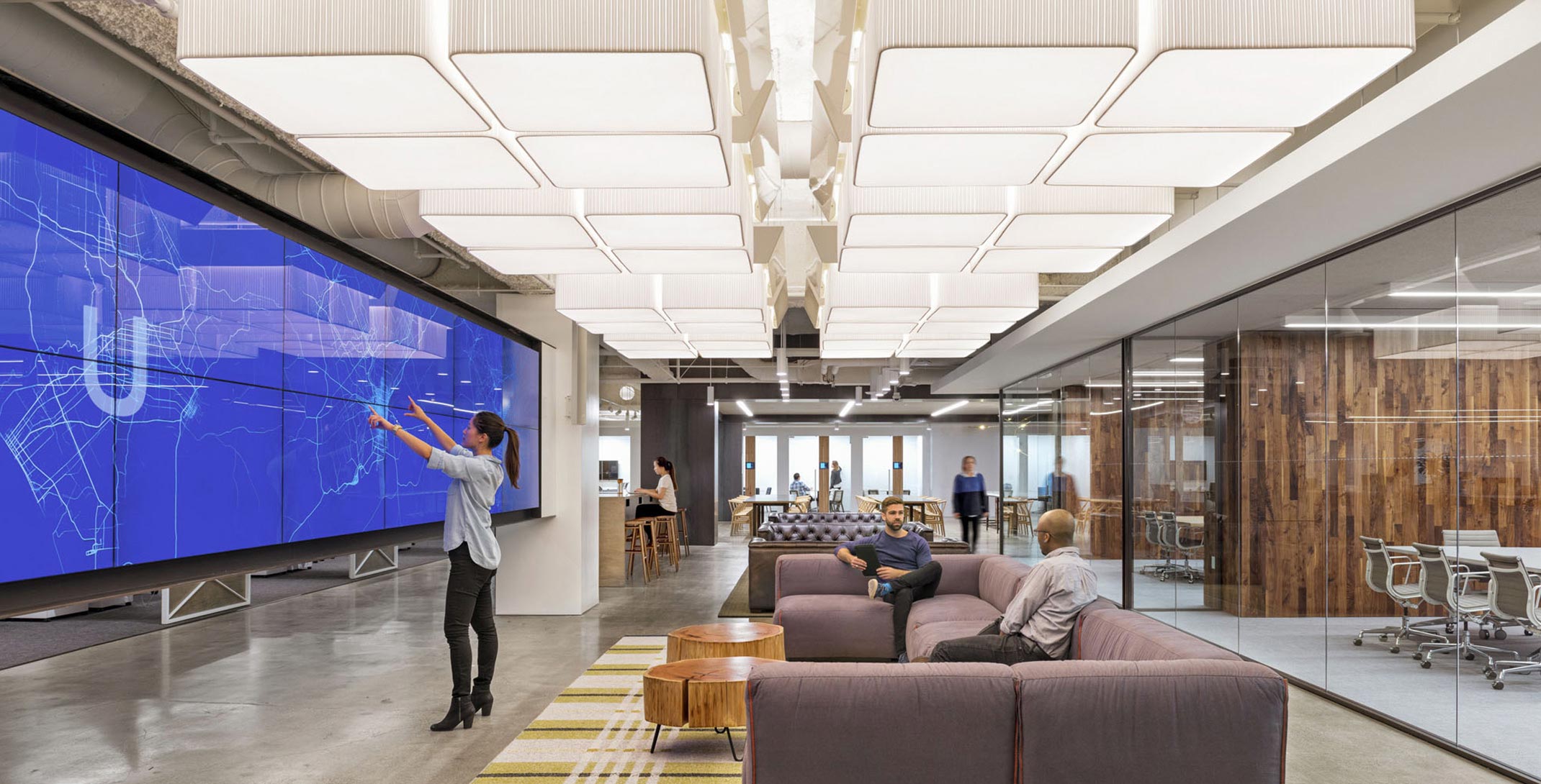 The interior, communal space of Uber's Headquarters, with employees sitting in oversized sofas and looking at large TV monitors